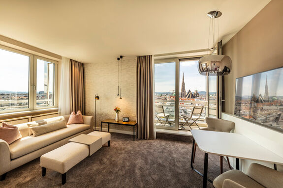 Eine Couch und ein Tisch mit zwei Sesseln befindet sich in der Suite im Hotel am Parkring, die Balkontür steht offen und zwei Sessel stehen draußen. Von hieraus hat der Besucher einen fantastischen Blick zum Stephansdom.