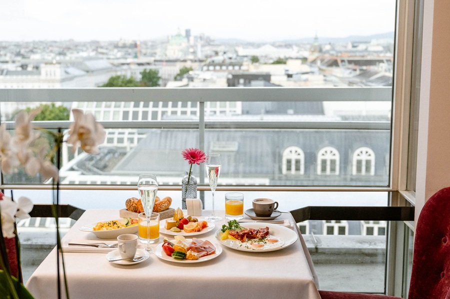 Blick in den Frühstücksraum mit mehreren gedeckten Tischen vor einem großen Glasfenster