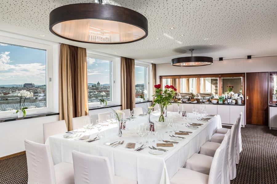 Tagen & Feiern Ein feierlich gedeckter Tisch in einem modern gestalteten Raum mit großen Fenstern und einem Panoramablick auf Wien