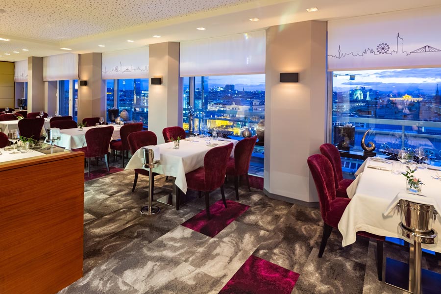 Hoch Genuss. Blick in das Restaurant Das Schick mit mehreren gedeckten Tischen vor einem großen Glasfenster